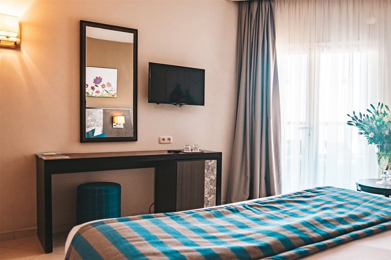 Ein Hotelzimmer mit Bett, Schreibtisch, Fernseher und einem Fenster mit Vorhängen.