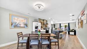 Een moderne keuken met houten kastjes, een eethoek met een tafel en stoelen, en een schilderij aan de muur.