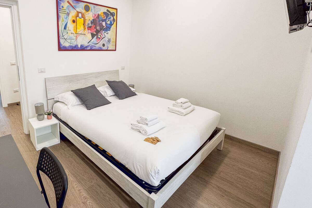 Ein ordentlich eingerichtetes Schlafzimmer mit Bett, Nachttisch, Stuhl und einem Bild an der Wand.