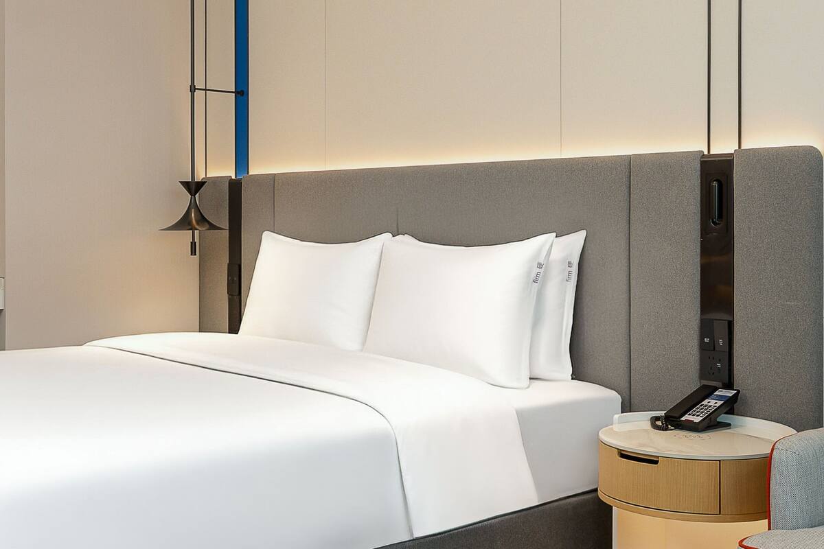 Camera d'albergo moderna con un letto grande, un comodino con il telefono e un pannello di controllo a parete.