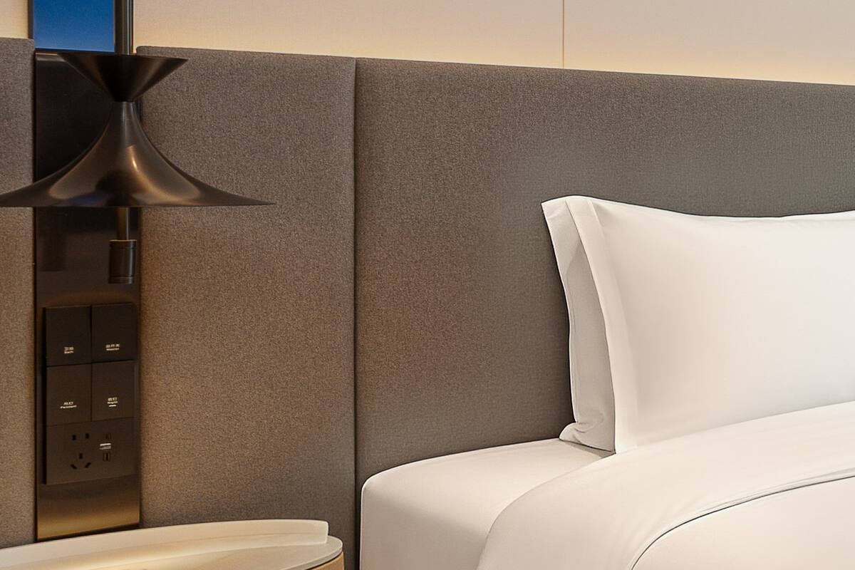 Una camera d'albergo moderna con un letto rifatto, una presa a muro e una lampada da terra contemporanea.