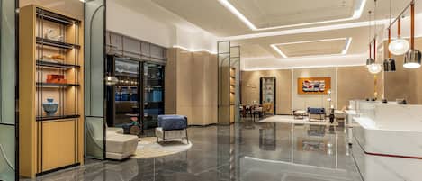 A modern hotel lobby with a marble floor, a reception desk, seating area, and a glass display cabinet.