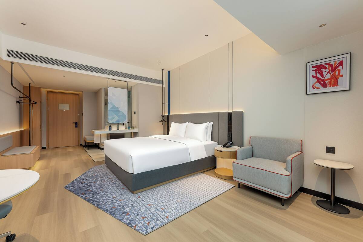 Una camera d'albergo moderna con un letto grande, un comodino, una sedia e un piccolo tavolino rotondo.