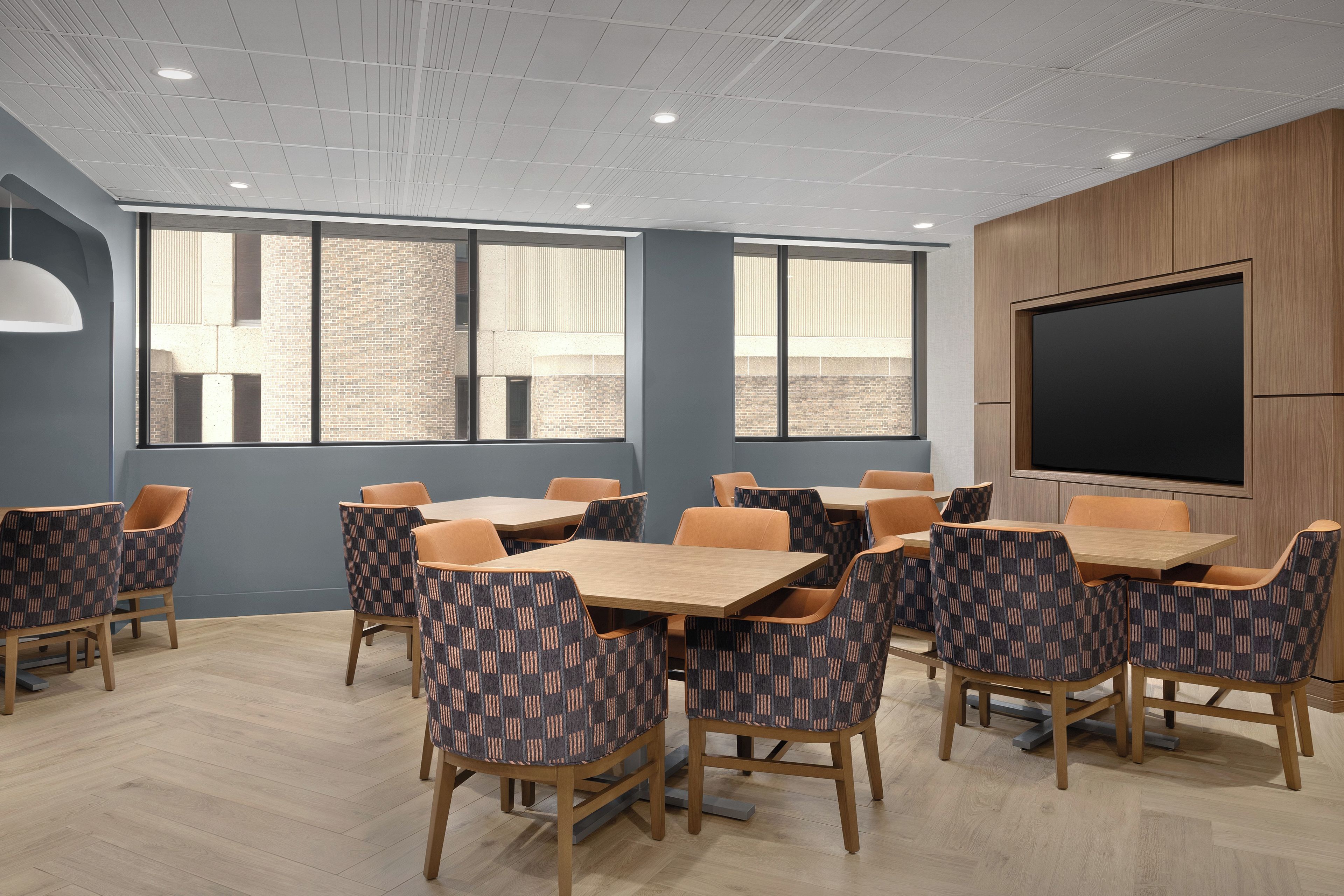A conference room with a large screen, multiple tables, and patterned chairs.