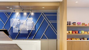 A hotel reception area with a modern design, including a blue geometric wall pattern, a reception desk, and a snack shelf. - Holiday Inn Express Knoxville Downtown by IHG (Knoxville)