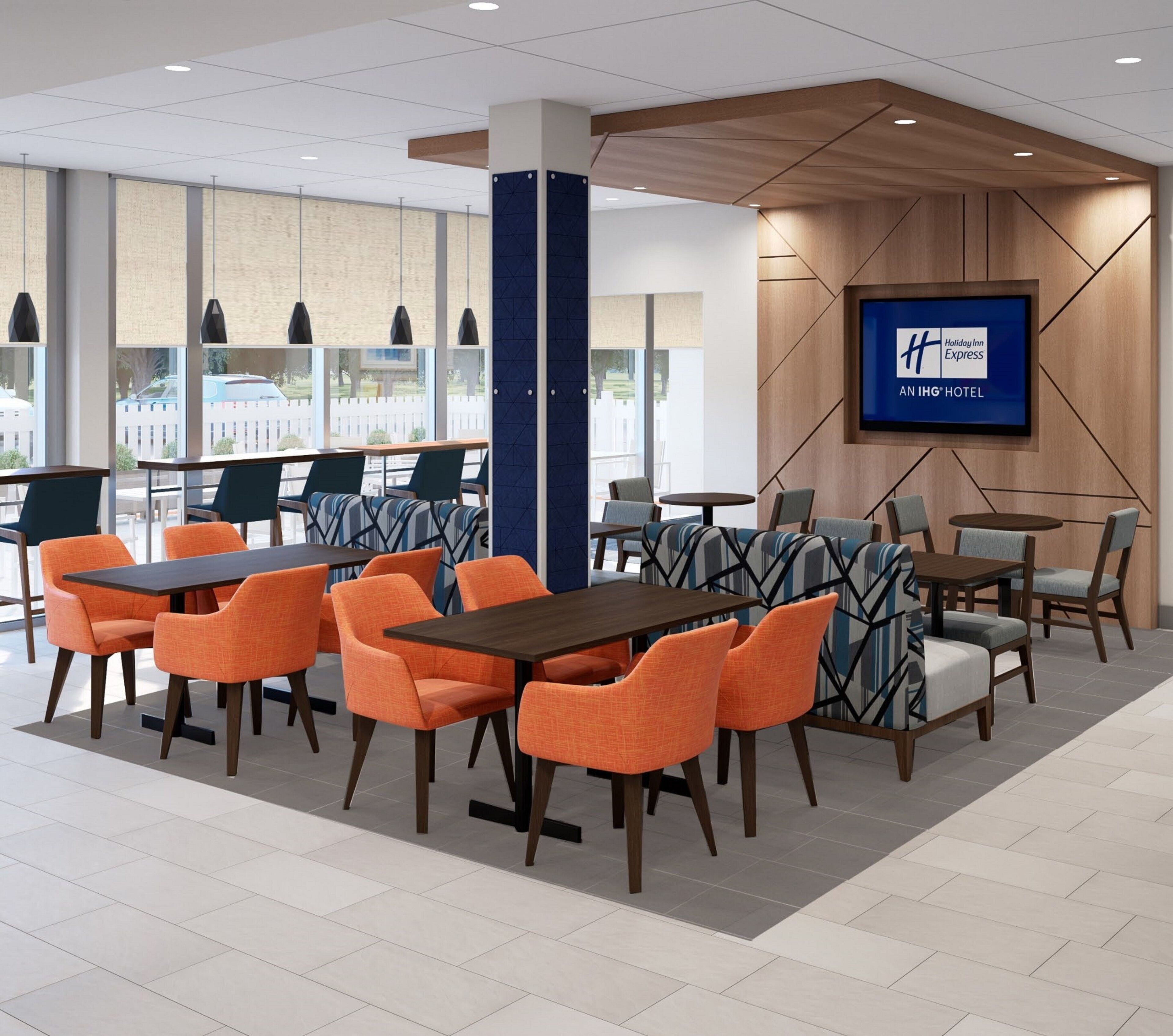 A hotel lobby with tables and chairs, a large TV screen, and a view of the outside.