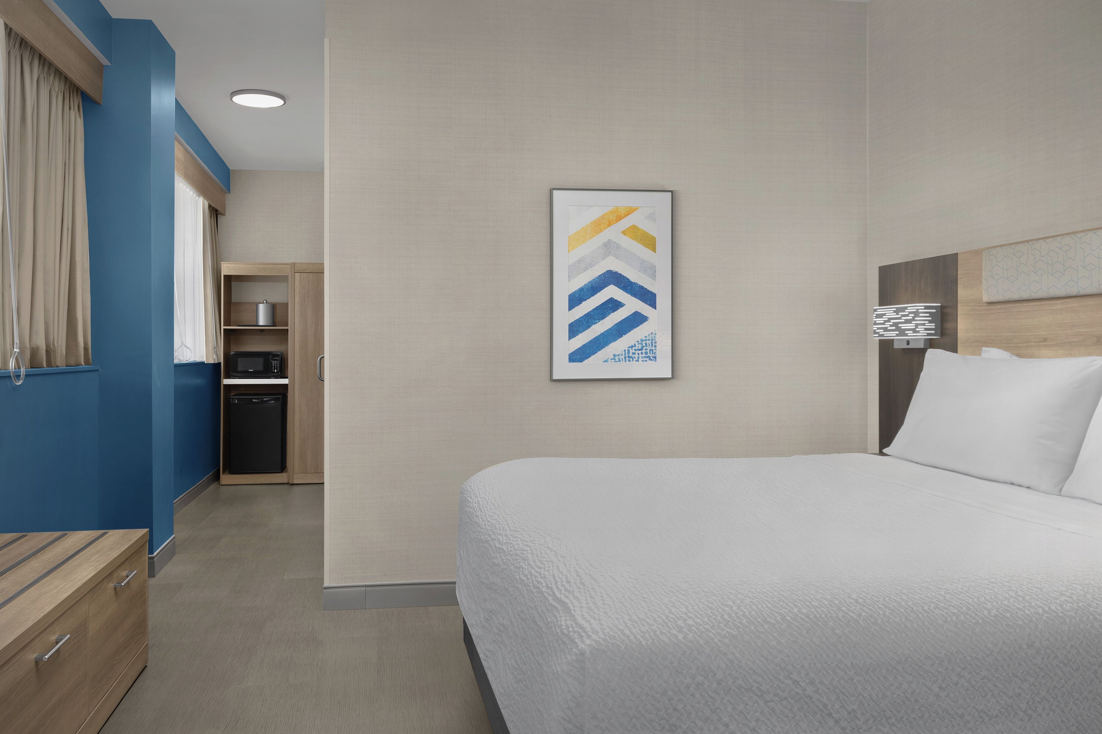 A hotel room with a bed, a small kitchenette, and a bathroom.