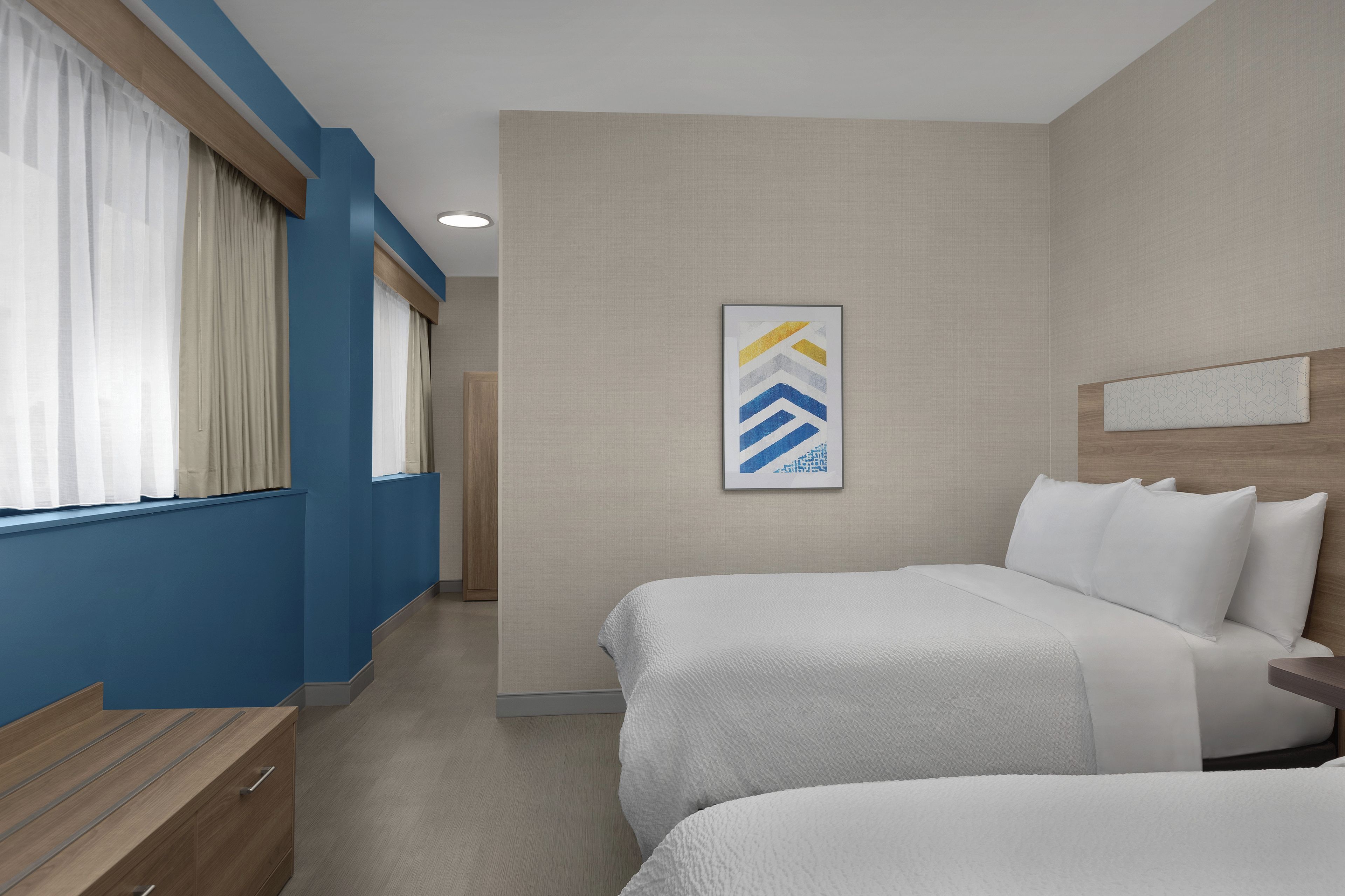A hotel room with two beds, a large window with curtains, a wall-mounted artwork, and a wooden headboard.