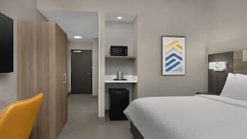 Habitación de hotel con cama, escritorio, silla, microondas y una pequeña kitchenette.