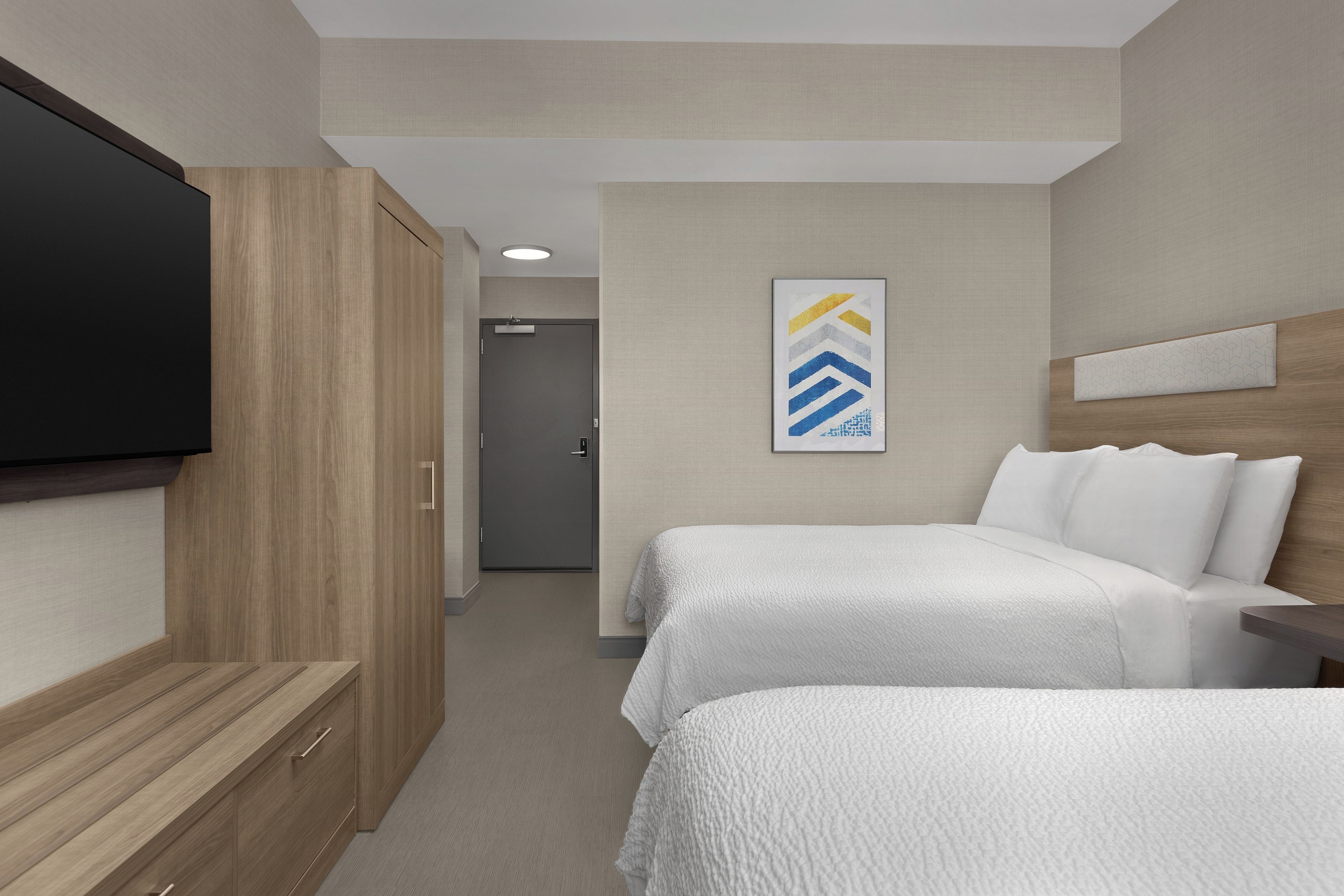 A hotel room with a bed, a TV, a desk, and a door leading to a hallway.