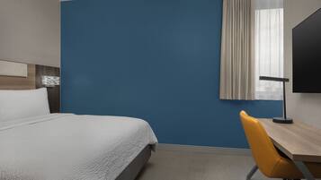 A hotel room with a bed, a desk, a chair, a TV, and a window with curtains.