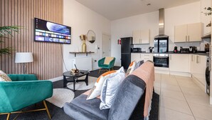 A modern living room with a sofa, a TV mounted on the wall, and a kitchen area with cabinets and appliances. - Spacious 2 bed apt Near Media City and Old Trafford (Salford)