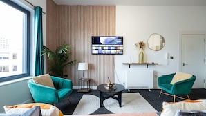A modern living room with teal armchairs, a central coffee table, and a flat-screen TV mounted on the wall. - Spacious 2 bed apt Near Media City and Old Trafford (Salford)