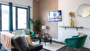 A modern living room with a sofa, two green armchairs, a coffee table, and a TV mounted on the wall. - Spacious 2 bed apt Near Media City and Old Trafford (Salford)