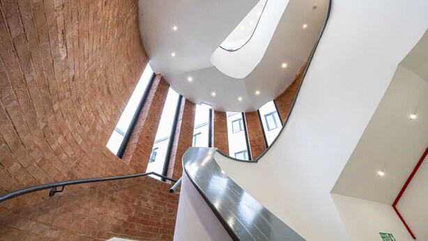 Een modern interieur met een gebogen trap, een bakstenen muur en een wit plafond met ingebouwde verlichting.