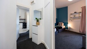 Een moderne hotelkamer met kitchenette, een bed met nachtkastje, een eettafeltje met lamp en een groot raam met gordijnen.