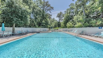 A clear swimming pool with lounge chairs and a fence, surrounded by trees.