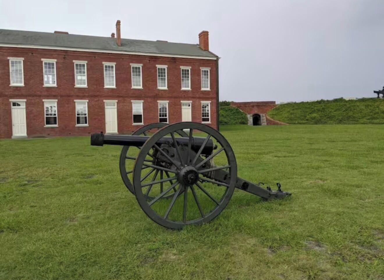 Un cannone in un prato erboso, con un edificio in mattoni sullo sfondo.