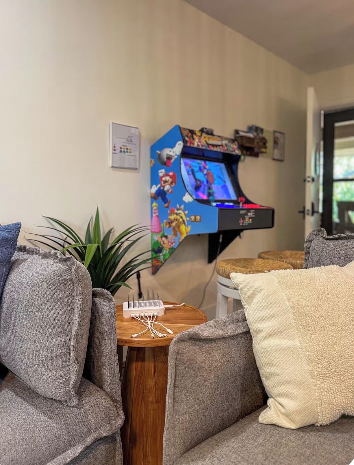 Una sala de estar con una consola de videojuegos, una planta y una pequeña mesa con un teclado.