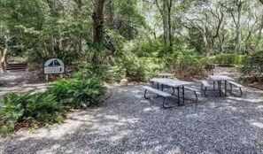 Une zone boisée équipée de tables de pique-nique et d’un panneau indiquant l’emplacement d’un terrain de camping.