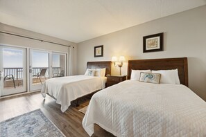 Ett hotellrum med två sängar, en balkong med stolar och utsikt över havet.