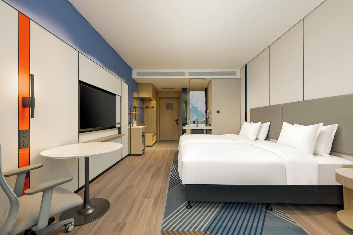 Una habitación de hotel moderna con una cama grande, un escritorio con silla, televisión y un baño visible a través de una puerta abierta.