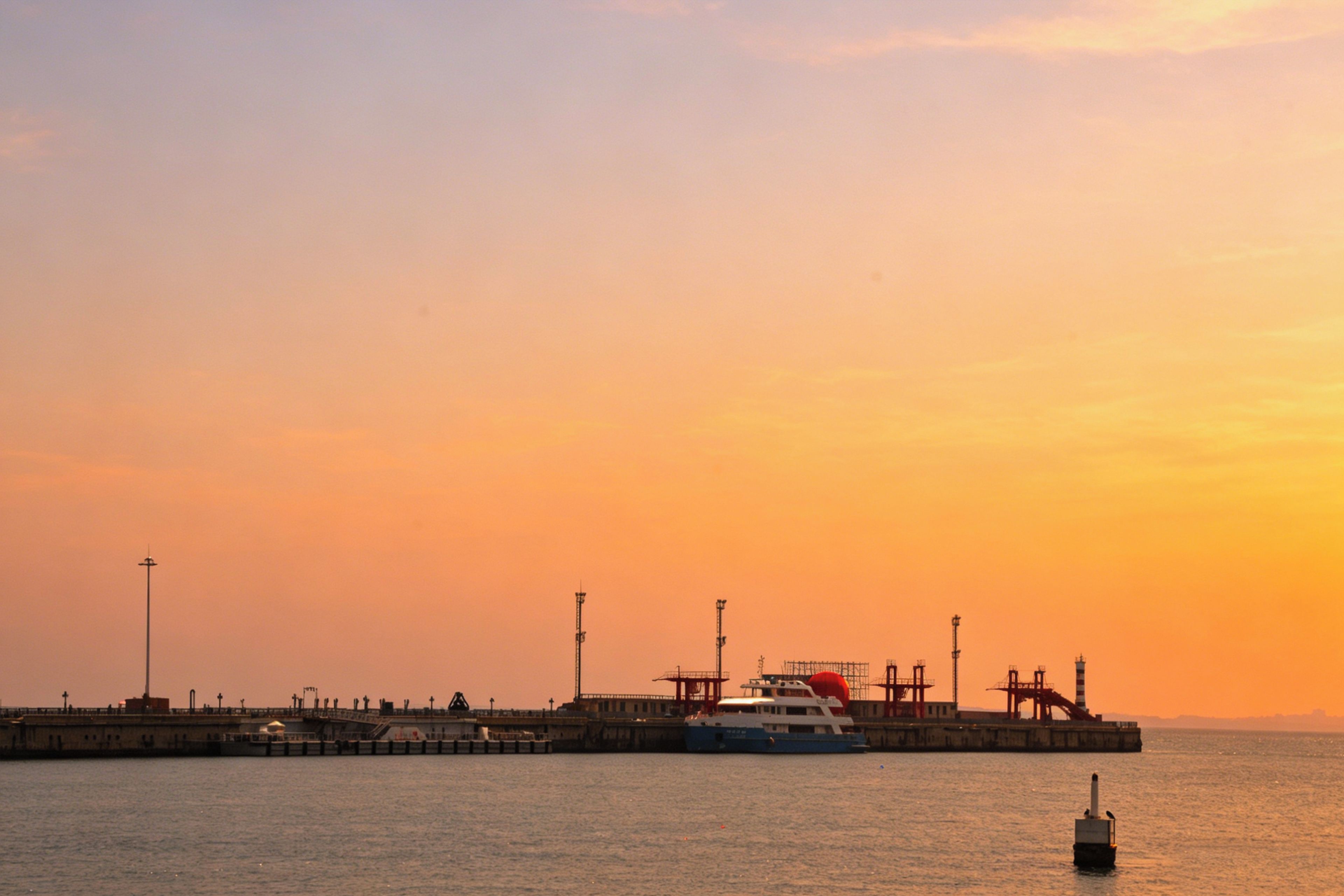 Una veduta sul lungomare con un molo, una barca e edifici industriali.