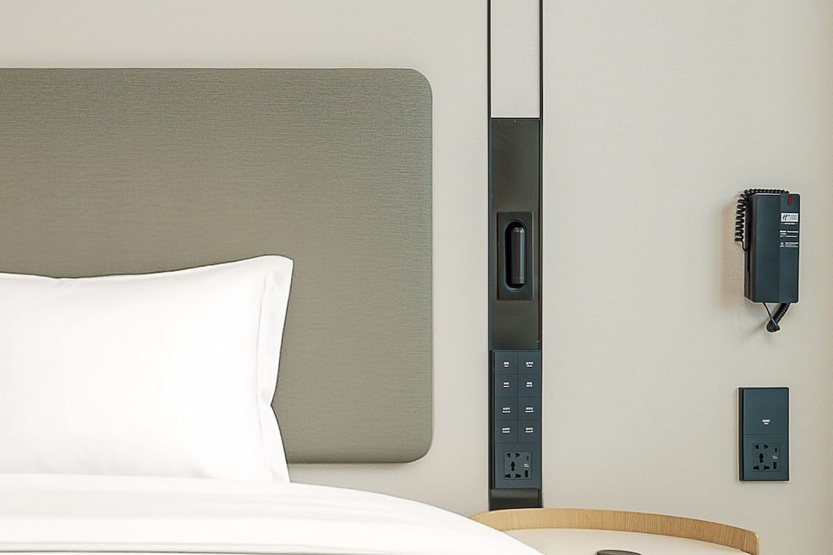 A hotel room with a bed, a wall-mounted phone, and a power outlet.