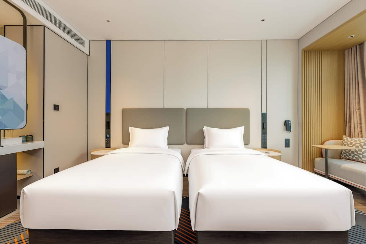 Ein Hotelzimmer mit zwei Einzelbetten, einem Schreibtisch mit Stuhl, einem kleinen Tisch und einem Sofa.