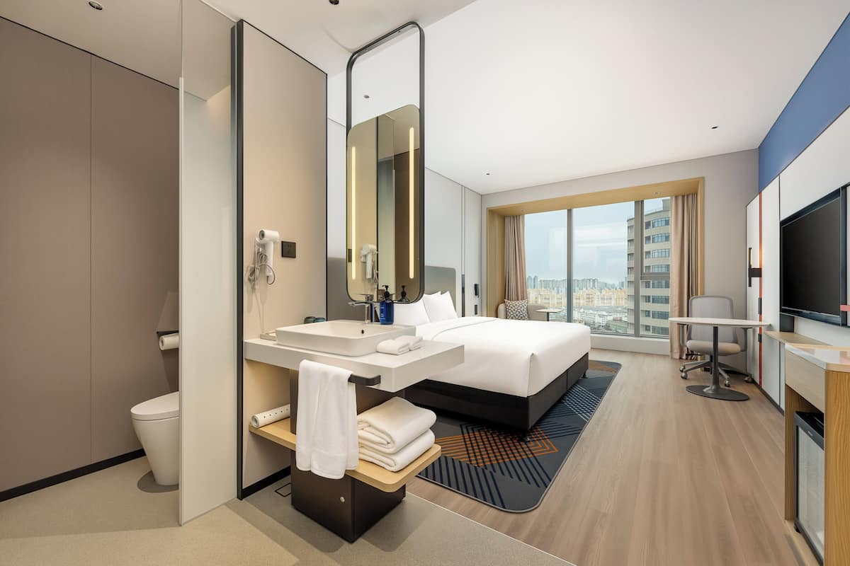 Una habitación de hotel moderna con una cama grande, baño independiente, un escritorio con silla y televisión.
