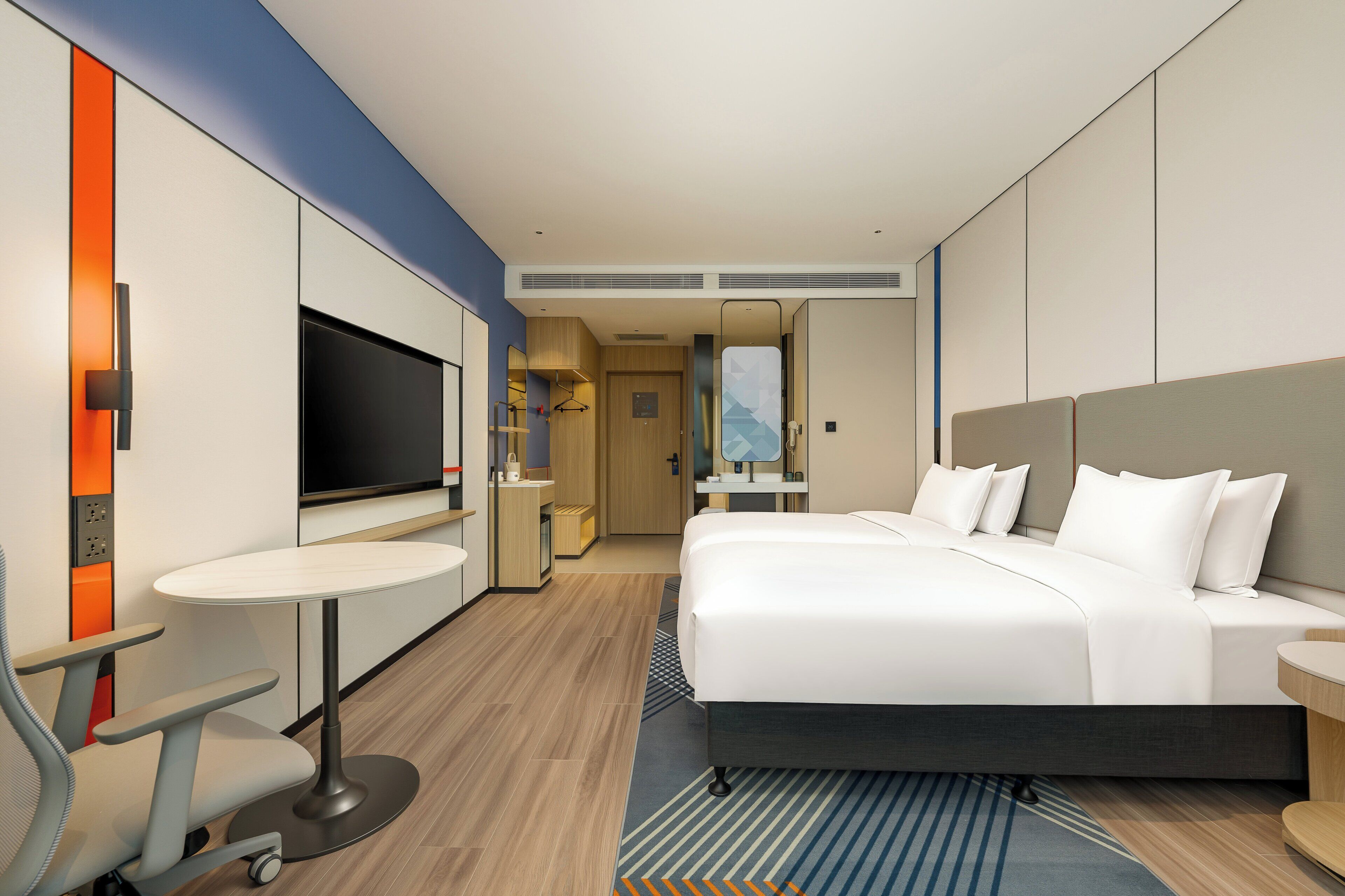 A modern hotel room with a large bed, a desk with a chair, a television, and a bathroom visible through an open door.