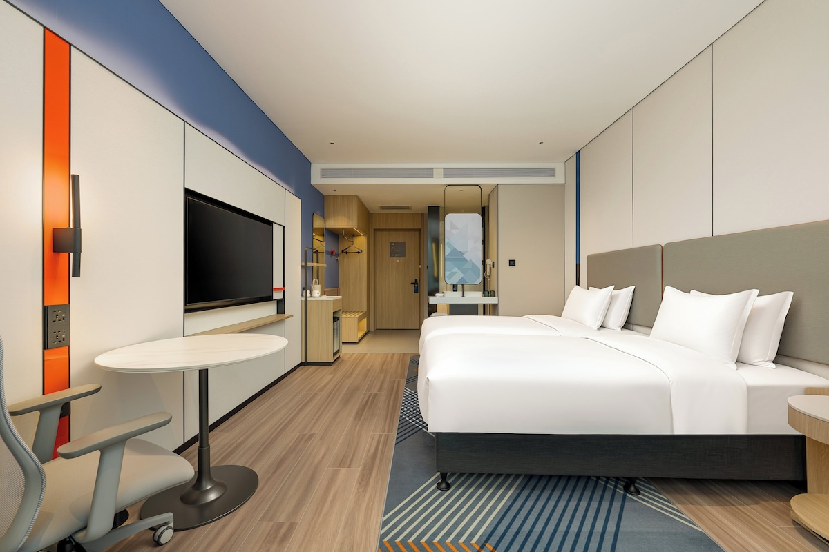Una habitación de hotel moderna con una cama grande, un escritorio con silla, televisión y un baño visible a través de una puerta abierta.