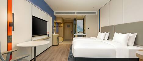 A modern hotel room with a large bed, a desk with a chair, a television, and a bathroom visible through an open door.