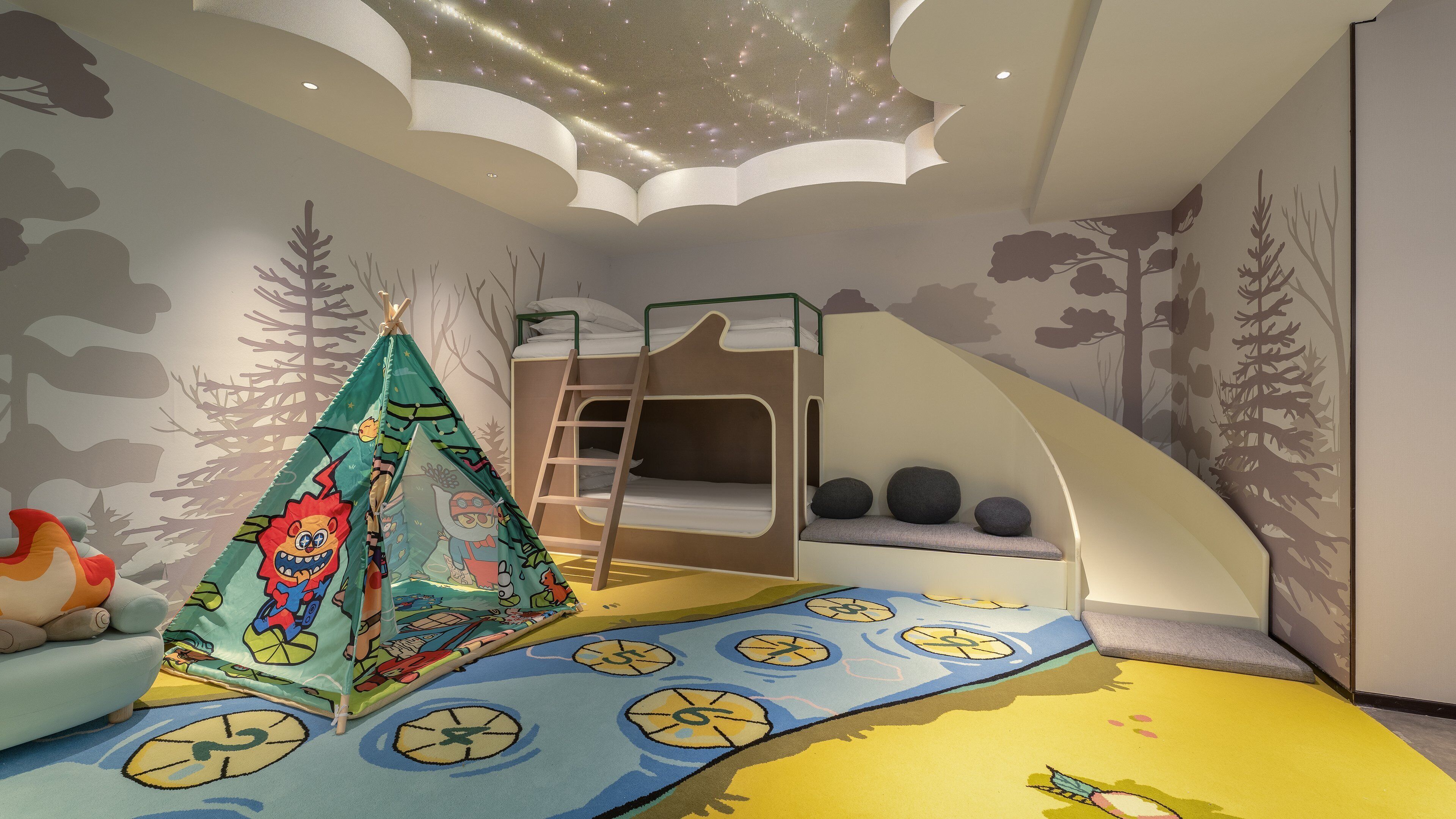 Une chambre d’enfant avec des lits superposés, une tente et un plafond décoré d’étoiles.
