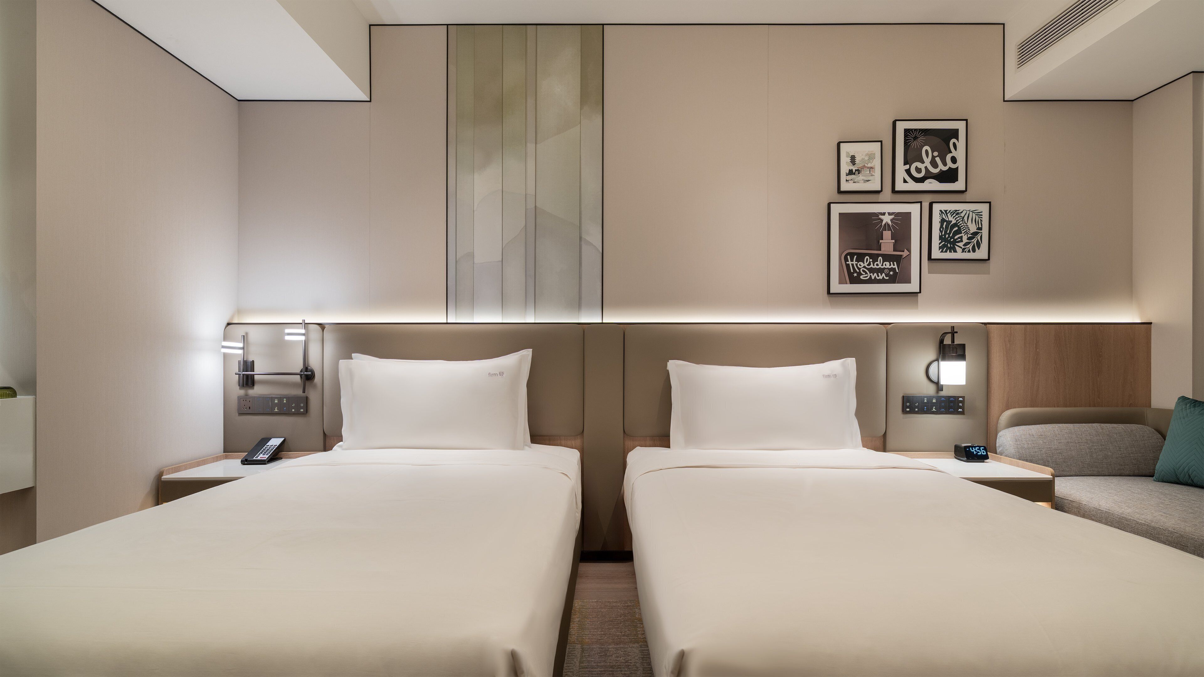 A hotel room with two beds, a nightstand with a phone, a coffee machine, and wall-mounted artwork.