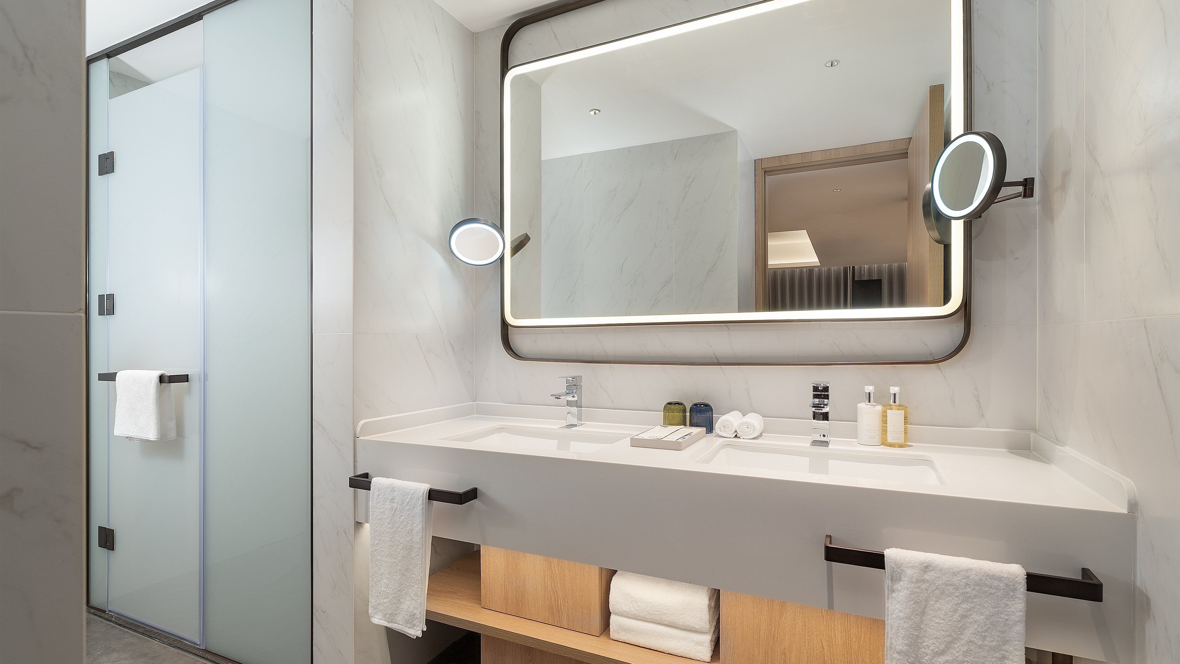 Ein modernes Badezimmer mit einem großen Spiegel, zwei Waschbecken und einer Duschkabine aus Glas.