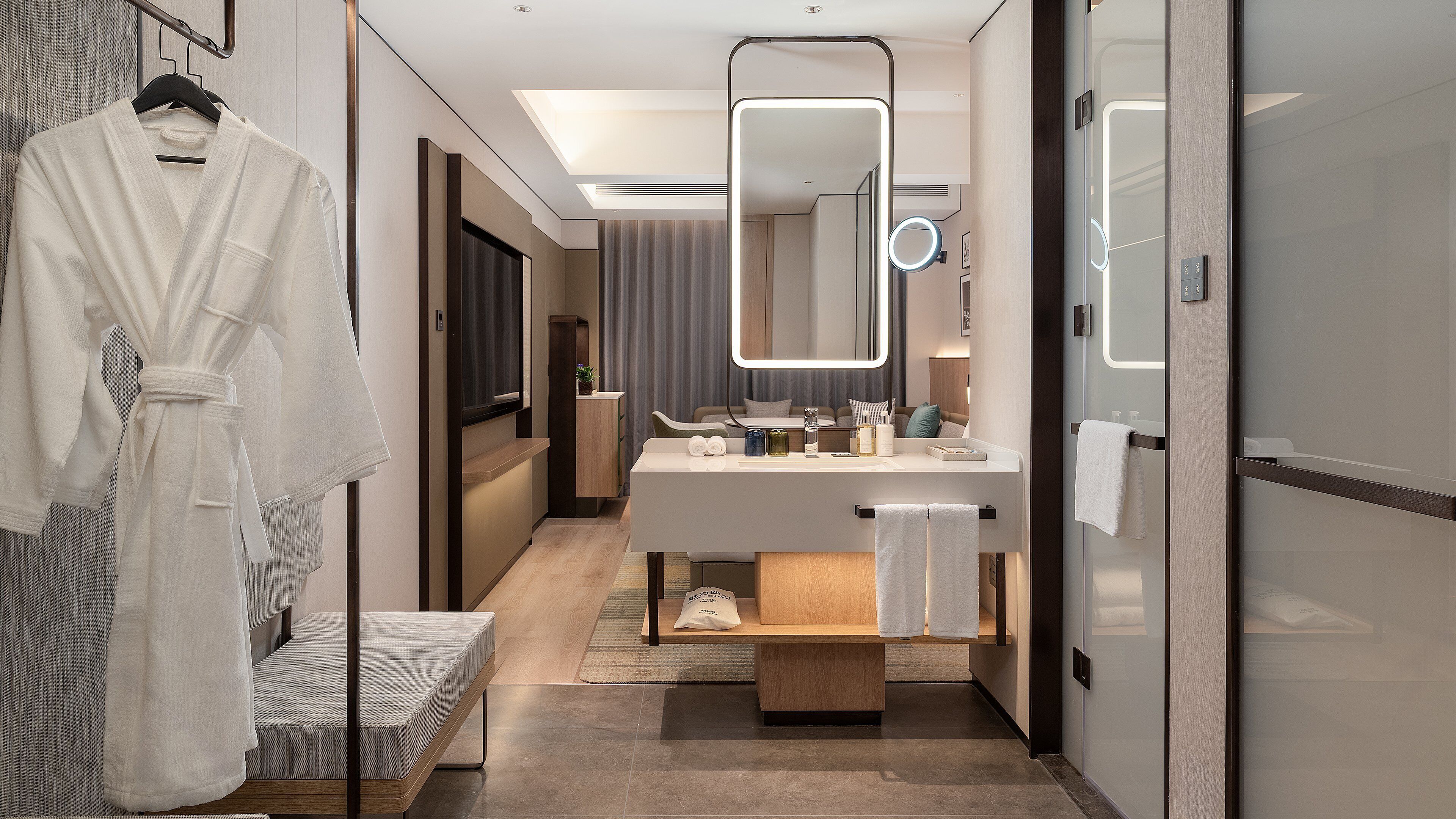 A modern hotel bathroom with a vanity, mirror, and a robe hanging on a rack.