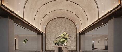 A spacious lobby with a high ceiling, a patterned wall, and a central floral arrangement.