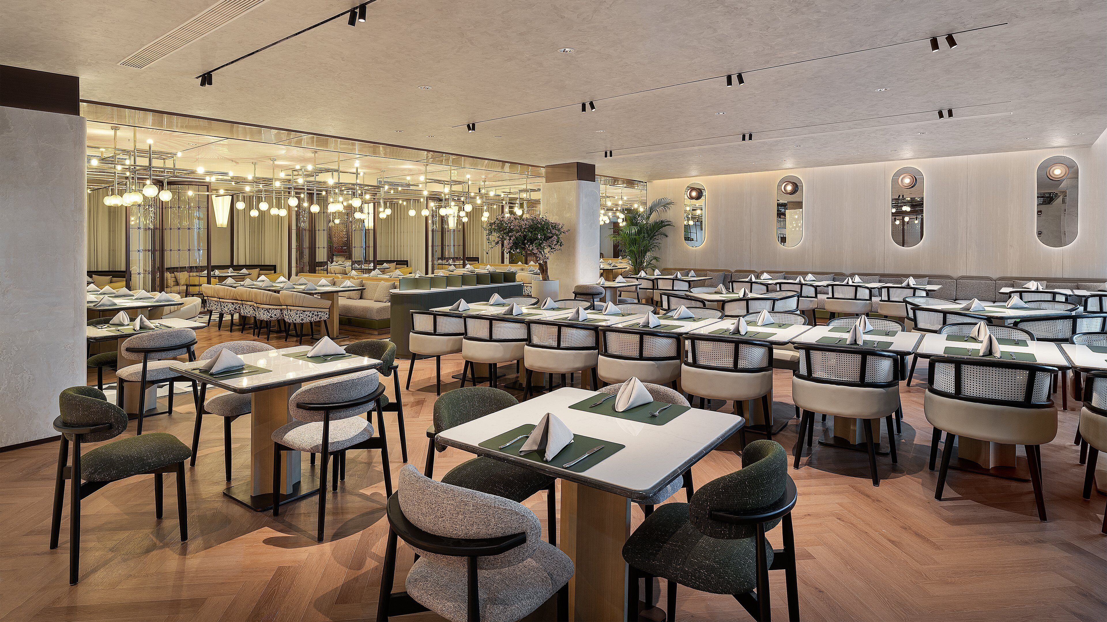 En rummelig restaurant med flere borde og stole, en moderne lysekrone og en stor spejlvæg.