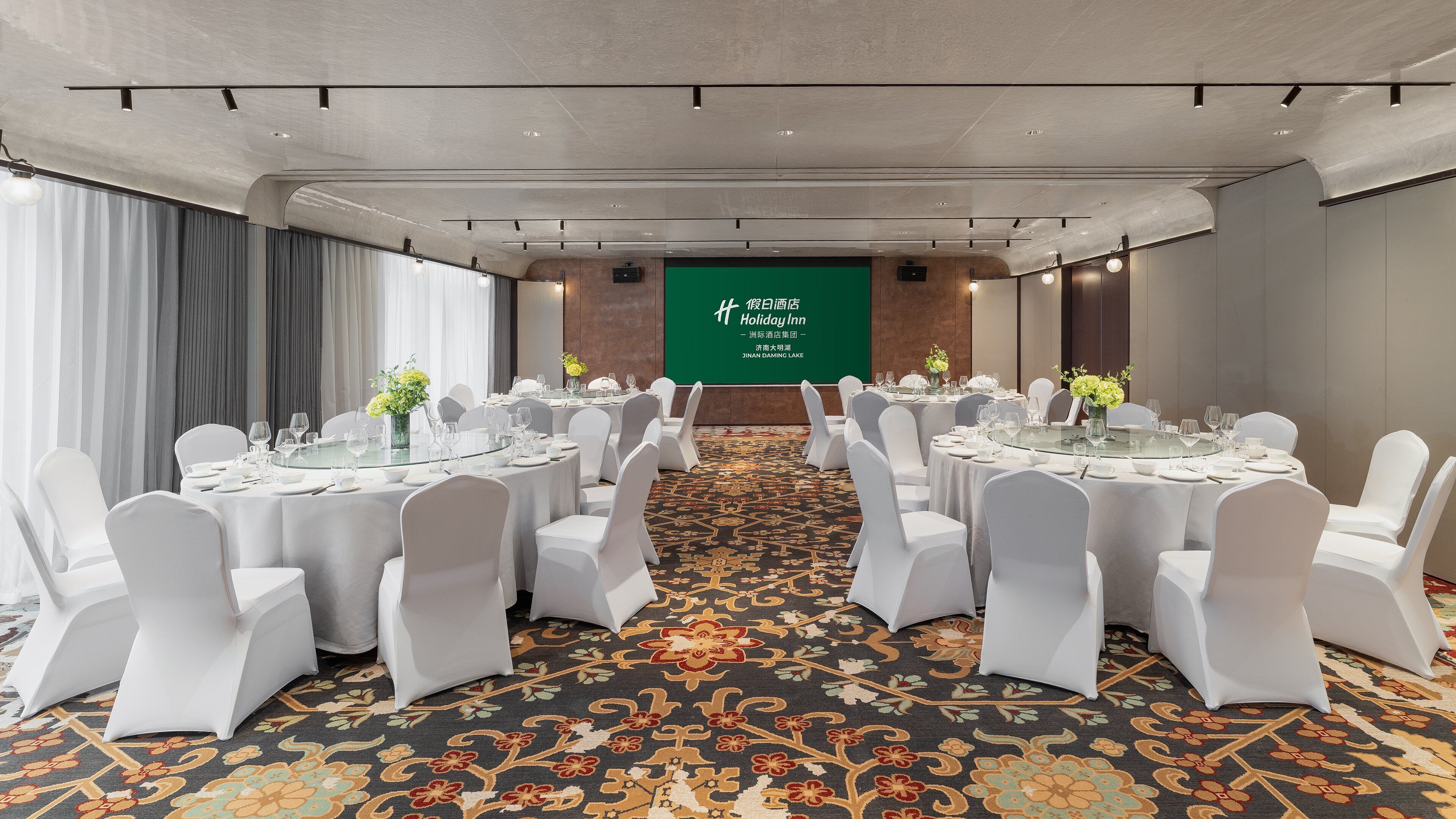 Un salón de conferencias con mesas redondas, sillas blancas y una pantalla de proyección.