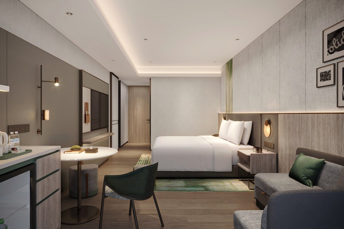 Une chambre d’hôtel moderne équipée d’un lit, d’un canapé, d’un bureau avec une chaise, d’une télévision et d’une salle de bain.