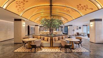Un vestíbulo moderno con una zona de estar central, un gran árbol y un mostrador de recepción.