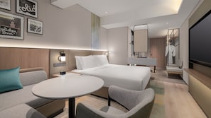 Ett modernt hotellrum med en säng, ett skrivbord, en stol, en TV och en spegel.