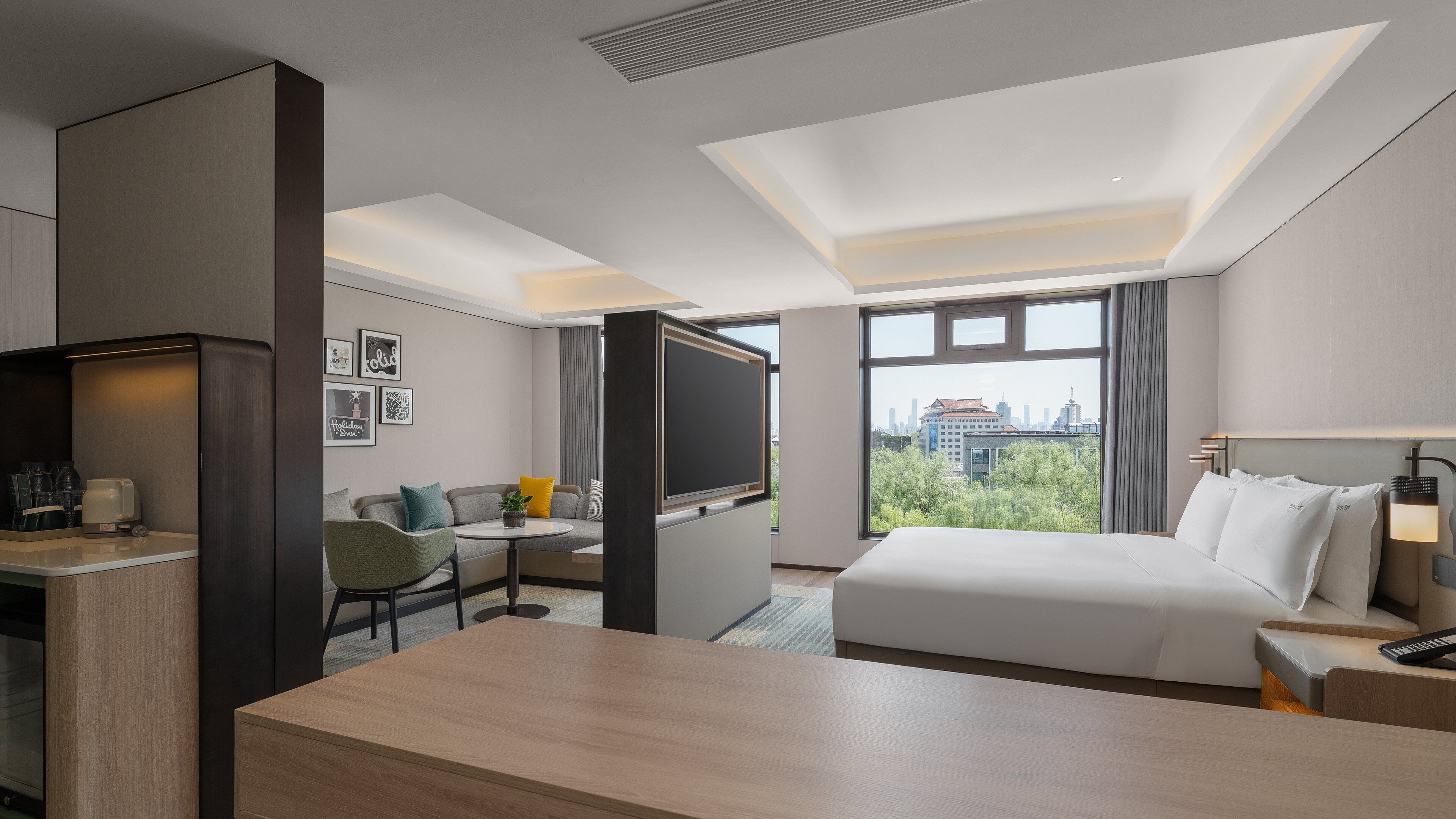 Ett hotellrum med en säng, ett skrivbord med en tv, en stol, ett litet bord och utsikt över stadsbilden.