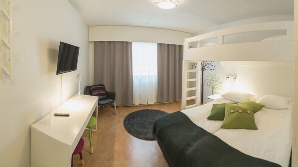 Quarto de hotel com cama, escrivaninha, cadeira, televisão e janela com cortinas.