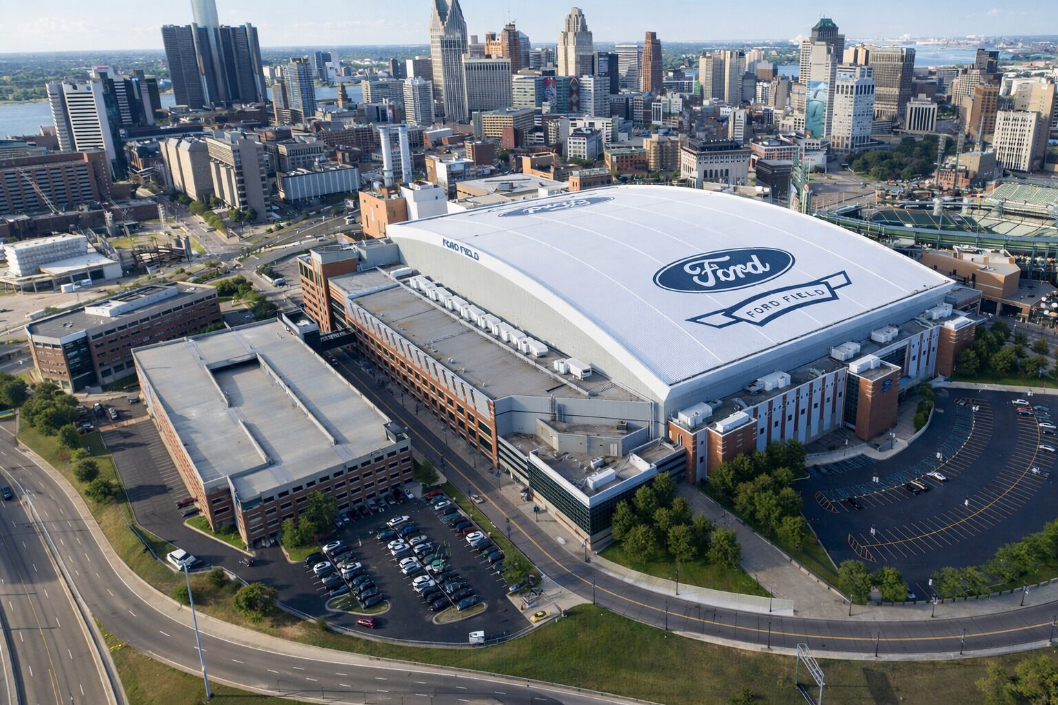 Ein großes Stadion mit einem gut sichtbaren Ford Field Logo, umgeben von Parkplätzen und einer Stadtkulisse im Hintergrund.
