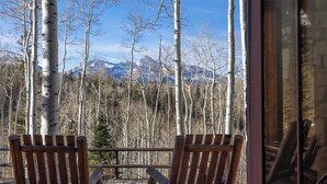 Due poltrone in legno di stile Adirondack rivolte verso una vista montana, con dei betuli sullo sfondo.