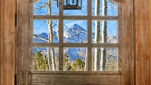 Una baita di legno con un'ampia finestra ad arco che si affaccia su montagne innevate e alberi di betulla.
