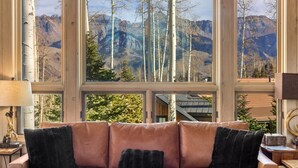 Una stanza con un'ampia finestra vista sulle montagne, un divano in pelle con cuscini neri e un pavimento in legno.