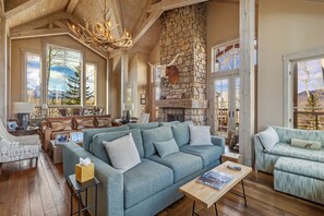 A cozy living room with a stone fireplace, large windows, and a comfortable seating area. - Luxurious 5-bedroom house in Mountain Village ideal for your getaway, any season (Mountain Village)